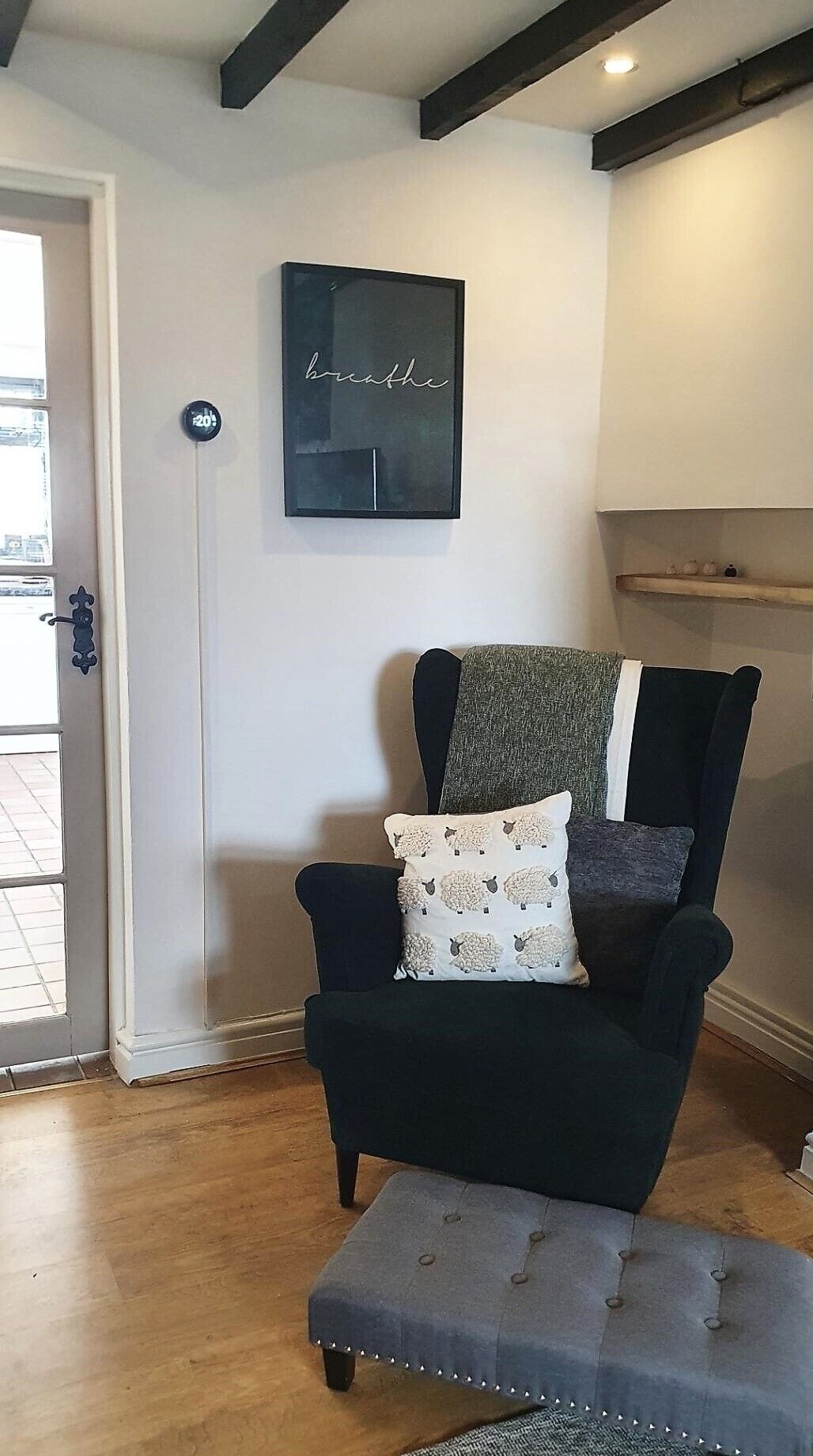 Un salón con un sillón oscuro, un pequeño reposapiés y un letrero en la pared con la palabra 'breathe'.