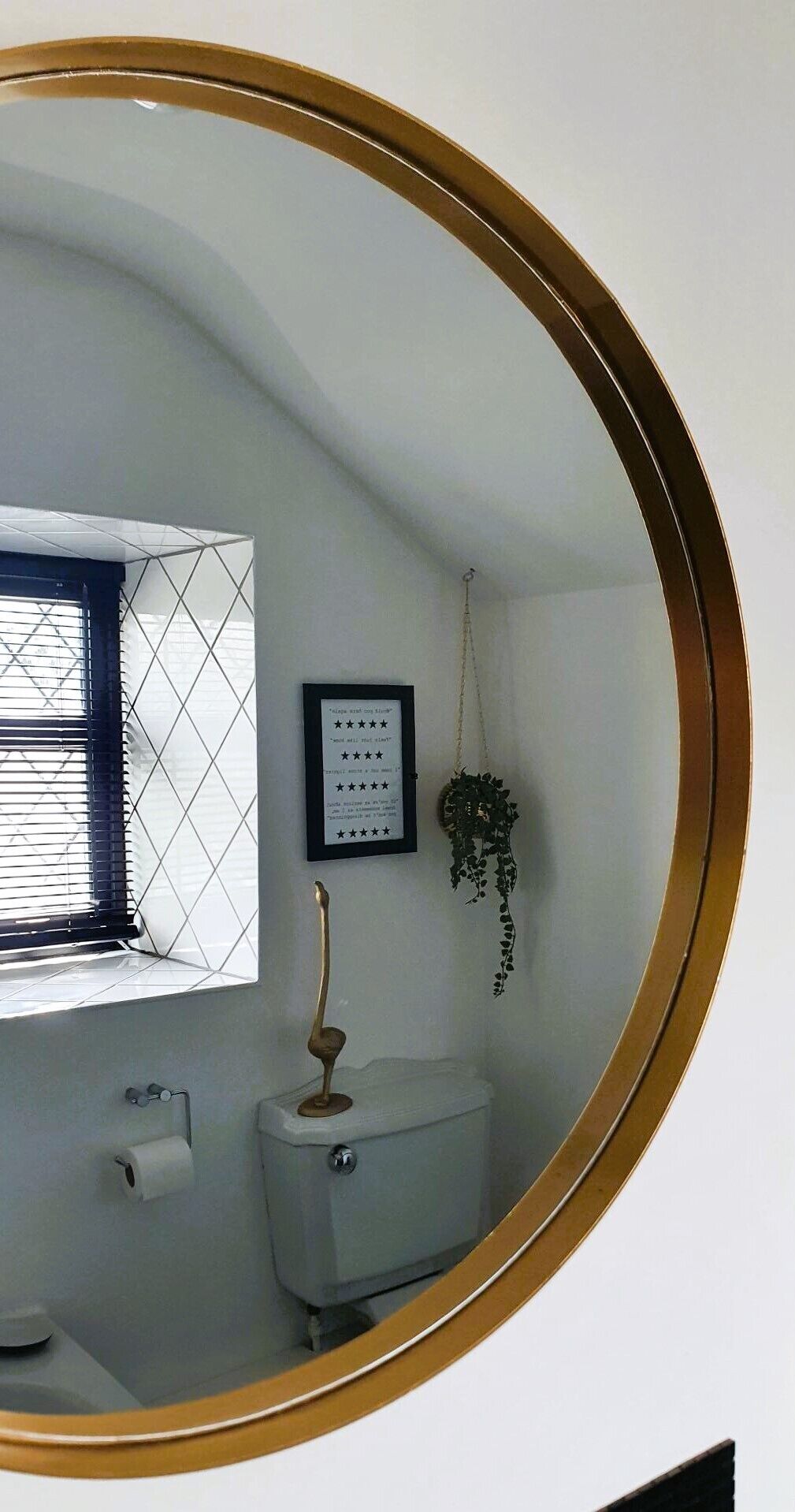 A bathroom with a toilet, a roll of toilet paper, a framed quote on the wall, and a hanging plant.
