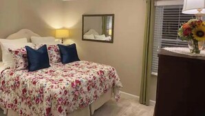 Una camera da letto con una coperta a fiori, una lampada da comodino, uno specchio e una finestra con tende.