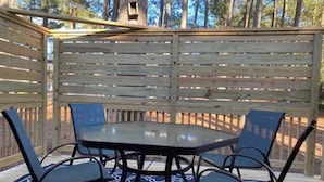 Un patio in legno con tavolo e sedie, circondato da una recinzione di legno e alberi.