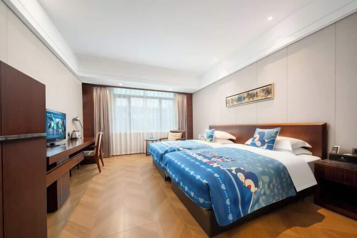 Una habitación de hotel con una cama grande, televisión, escritorio y ventana con cortinas.