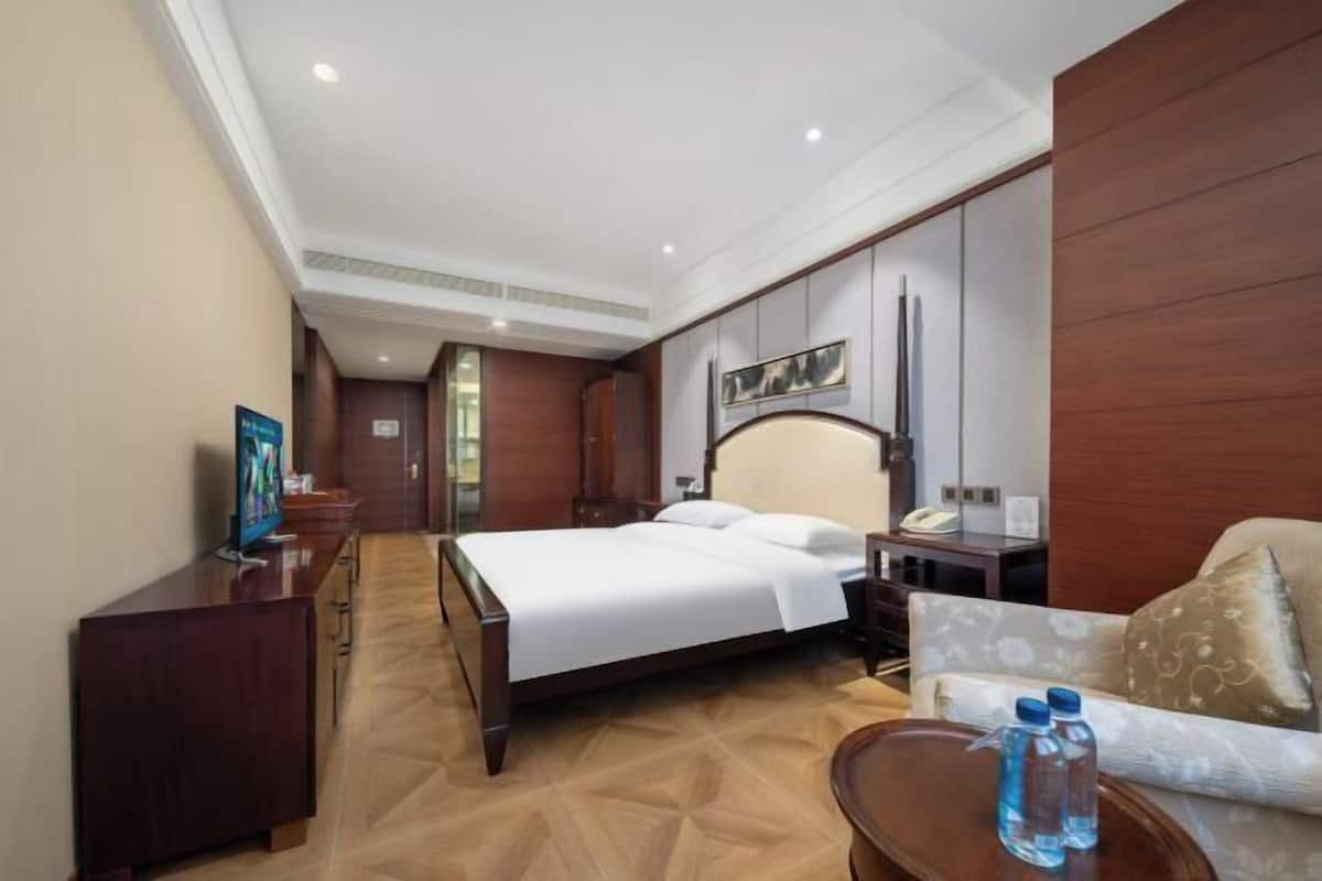 Una habitación de hotel con cama, mesita de noche, escritorio con silla, sofá y televisor.