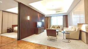 Una habitación de hotel moderna con piso de madera, un sofá, un televisor y un ventanal grande.