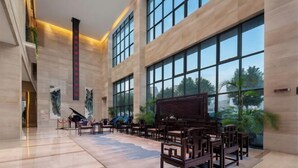 Un vestíbulo espacioso con un piano de cola, asientos cómodos, ventanas amplias y un diseño moderno.