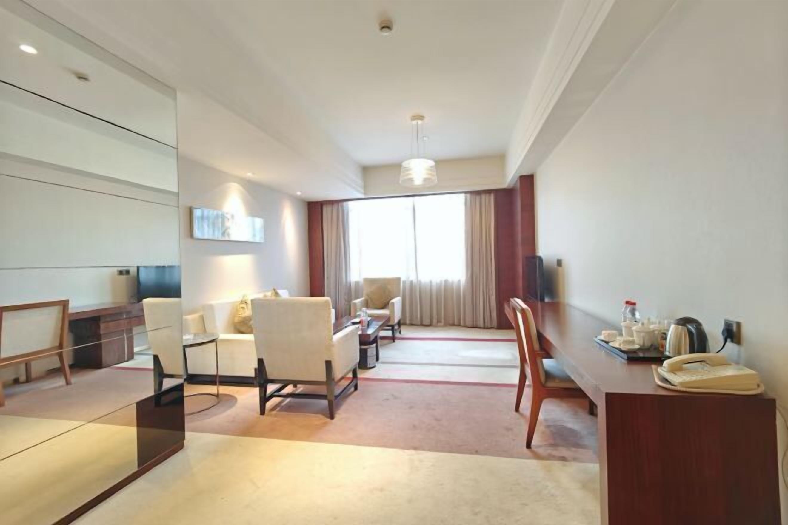 A modern hotel room with a dining area, a TV, a sofa, and a large window with curtains.