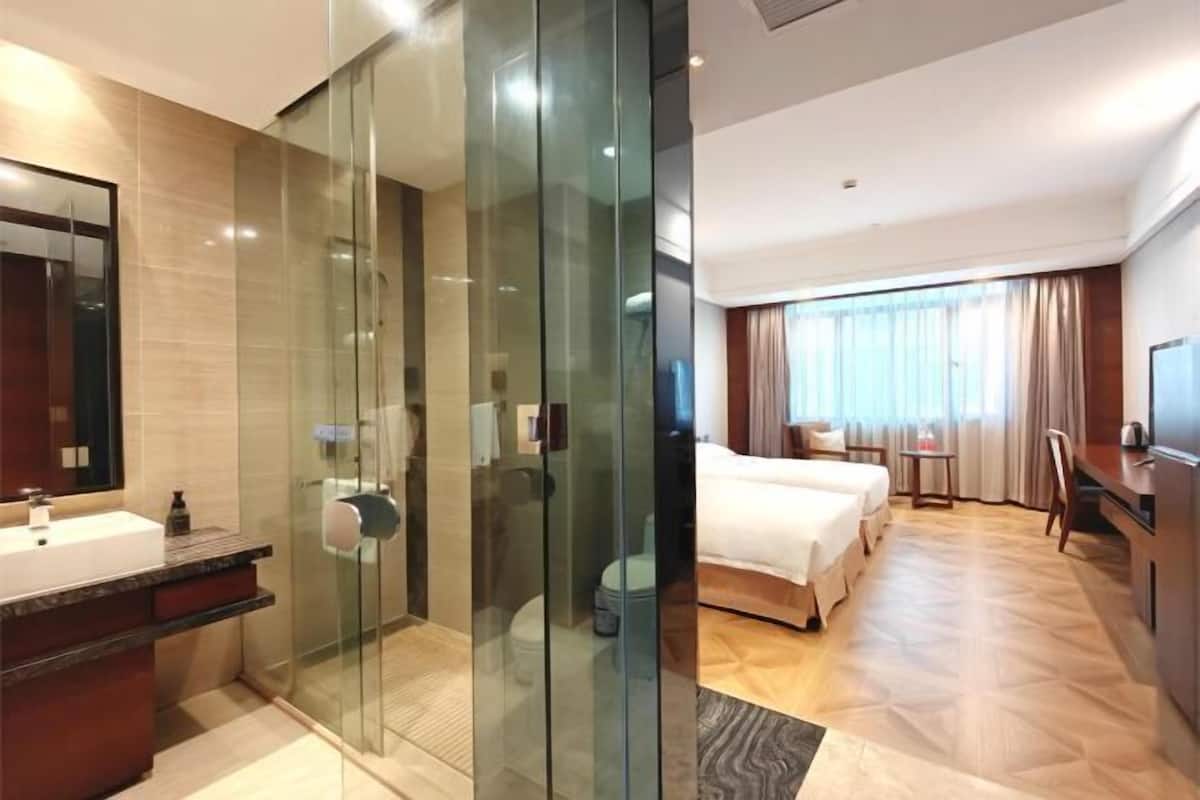 Una habitación de hotel moderna con ducha de vidrio, una cama grande, un escritorio y un televisor.