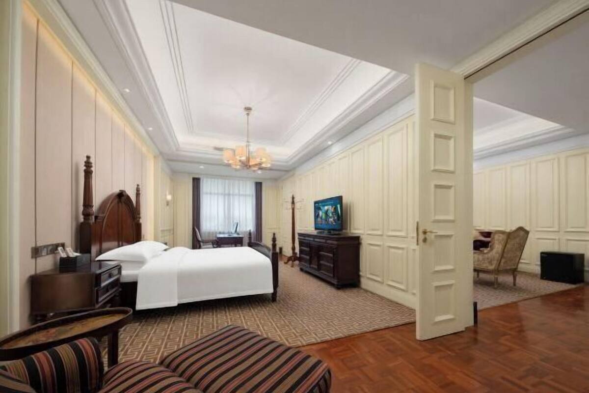 Una habitación de hotel espaciosa con una cama grande, televisión, cómoda de madera y una zona de estar con sofás a rayas.