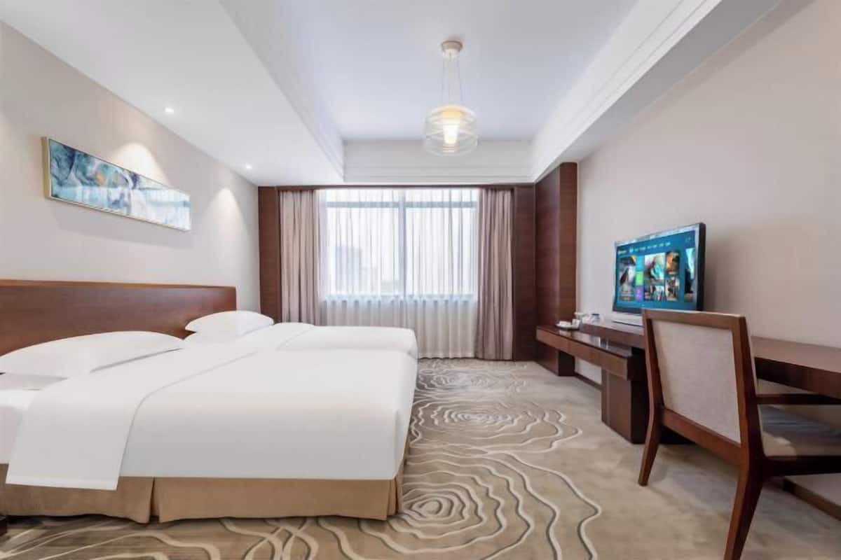 Una habitación de hotel con una cama grande, un escritorio con silla, televisor y ventana con cortinas.