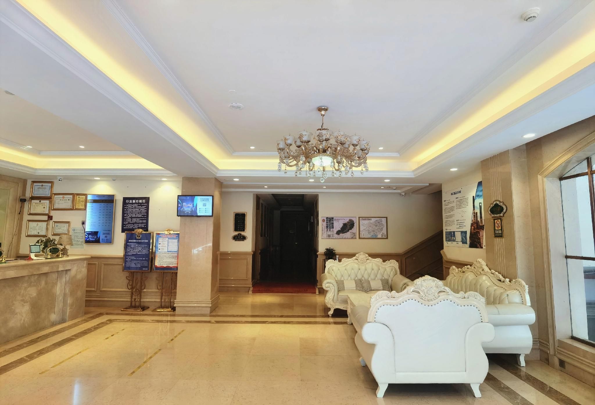 A lobby with a reception desk, framed certificates, a chandelier, and a seating area with ornate sofas.