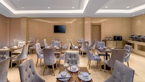 A hotel dining area with multiple tables and chairs, a flat-screen TV mounted on the wall, and a buffet station. - Vienna 3 Best Hotel (Guilin)