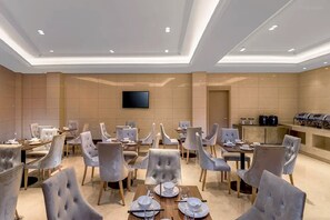 A hotel dining area with multiple tables and chairs, a flat-screen TV mounted on the wall, and a buffet station. - Vienna 3 Best Hotel (Guilin)