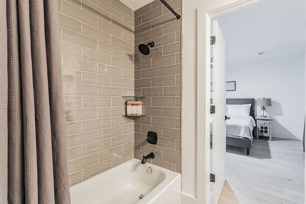 Une salle de bain moderne équipée d’une baignoire, d’une douche et d’une étagère en verre où sont rangés les articles de toilette.