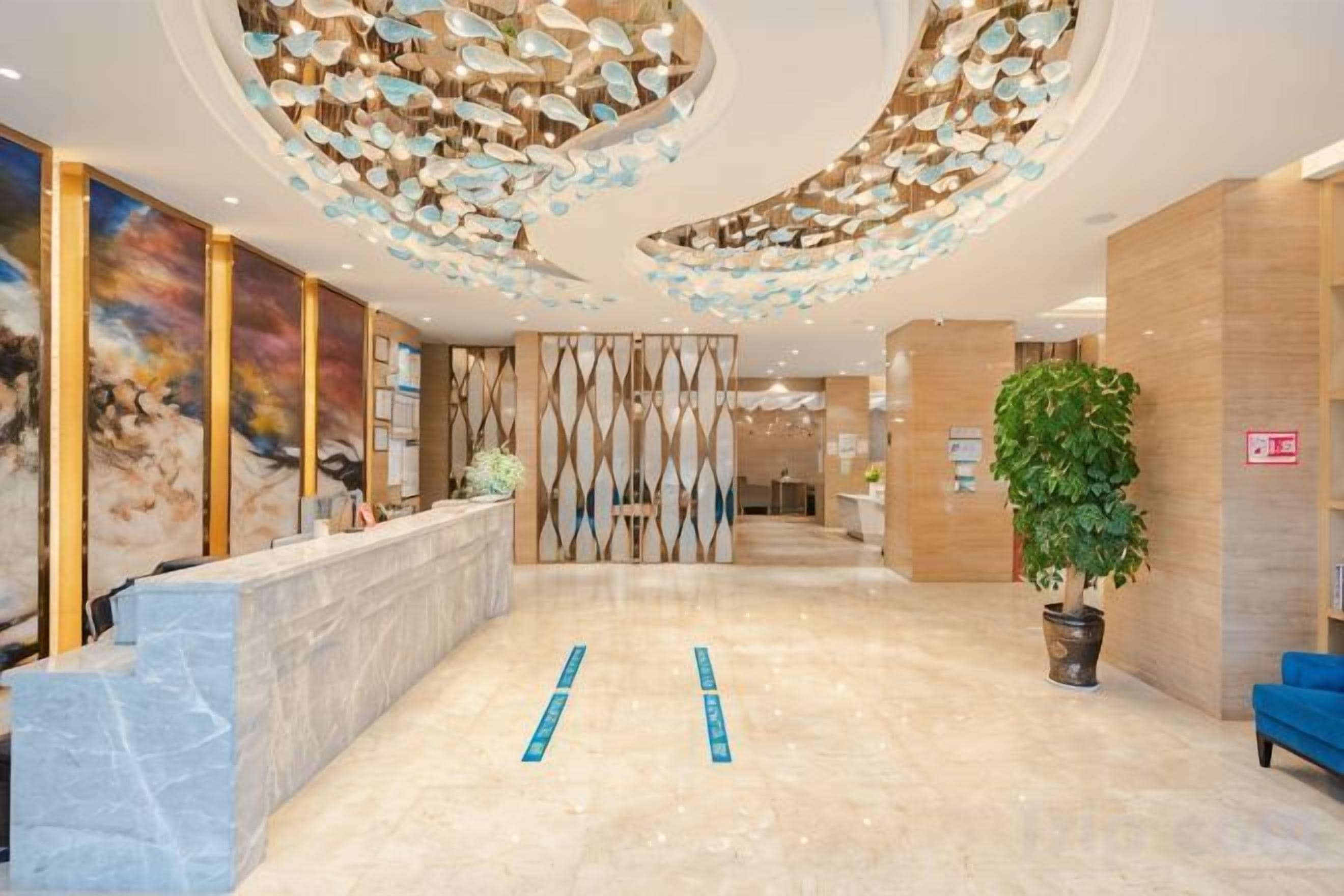Una hall d'albergo con una reception in marmo, un'ampia pianta in vaso e un moderno design del soffitto.