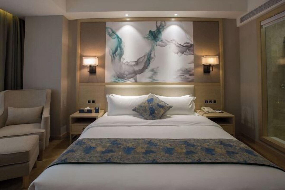 A hotel room with a large bed, two bedside tables, a chair, and a wall-mounted artwork.