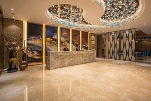 Un moderno vestíbulo de hotel con un mostrador de recepción de mármol, grandes pinturas abstractas y jarrones decorativos.