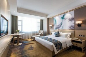 Habitación de hotel con una cama grande, un escritorio, una silla, una mesita y un cuadro en la pared.