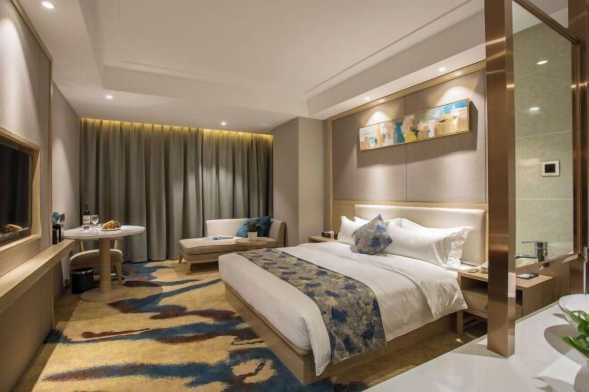 A modern hotel room with a large bed, a round table, a sofa, and a bathroom with a mirror.