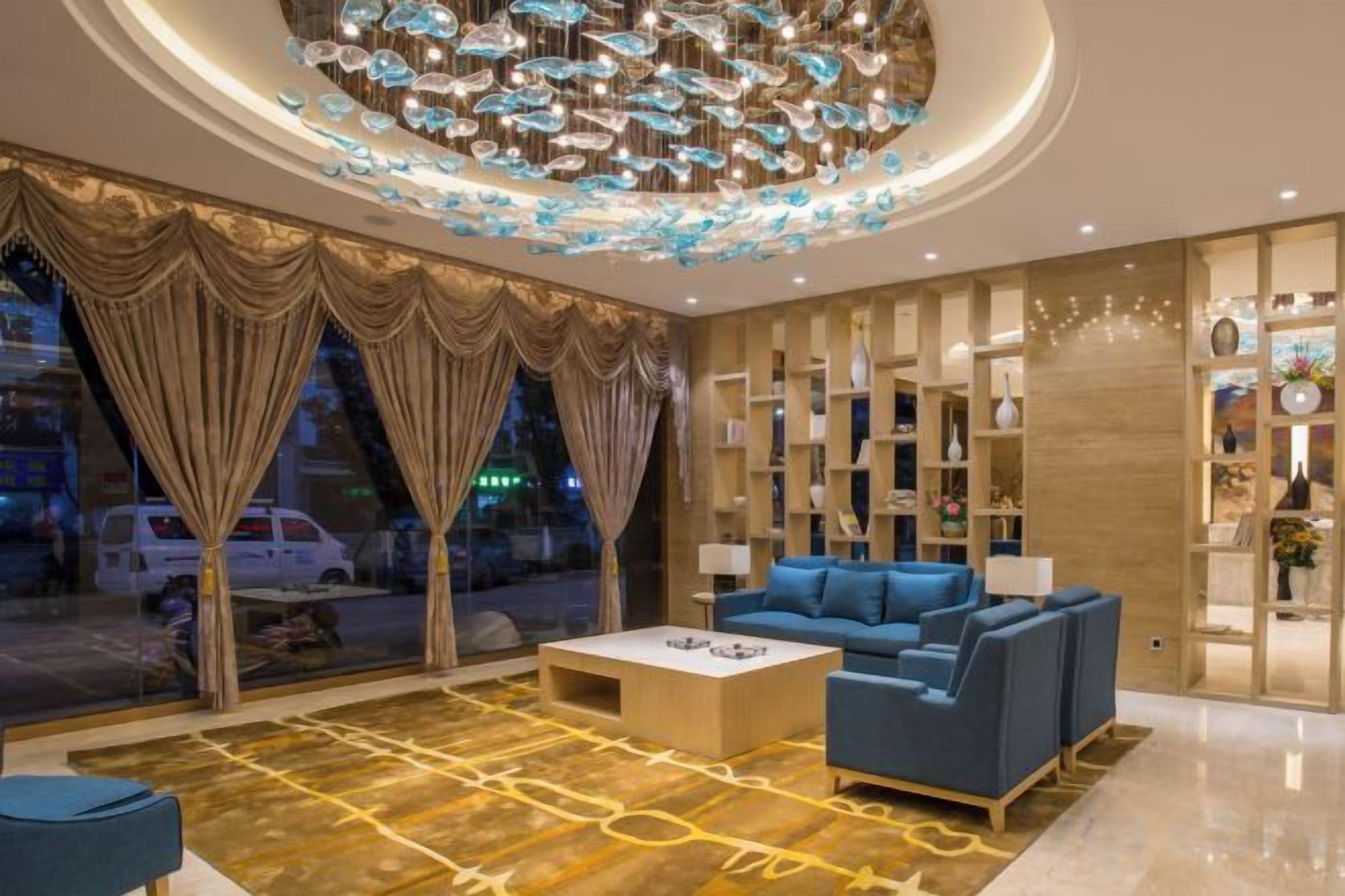 A modern hotel lobby with a blue sofa, a coffee table, and a decorative ceiling light fixture.