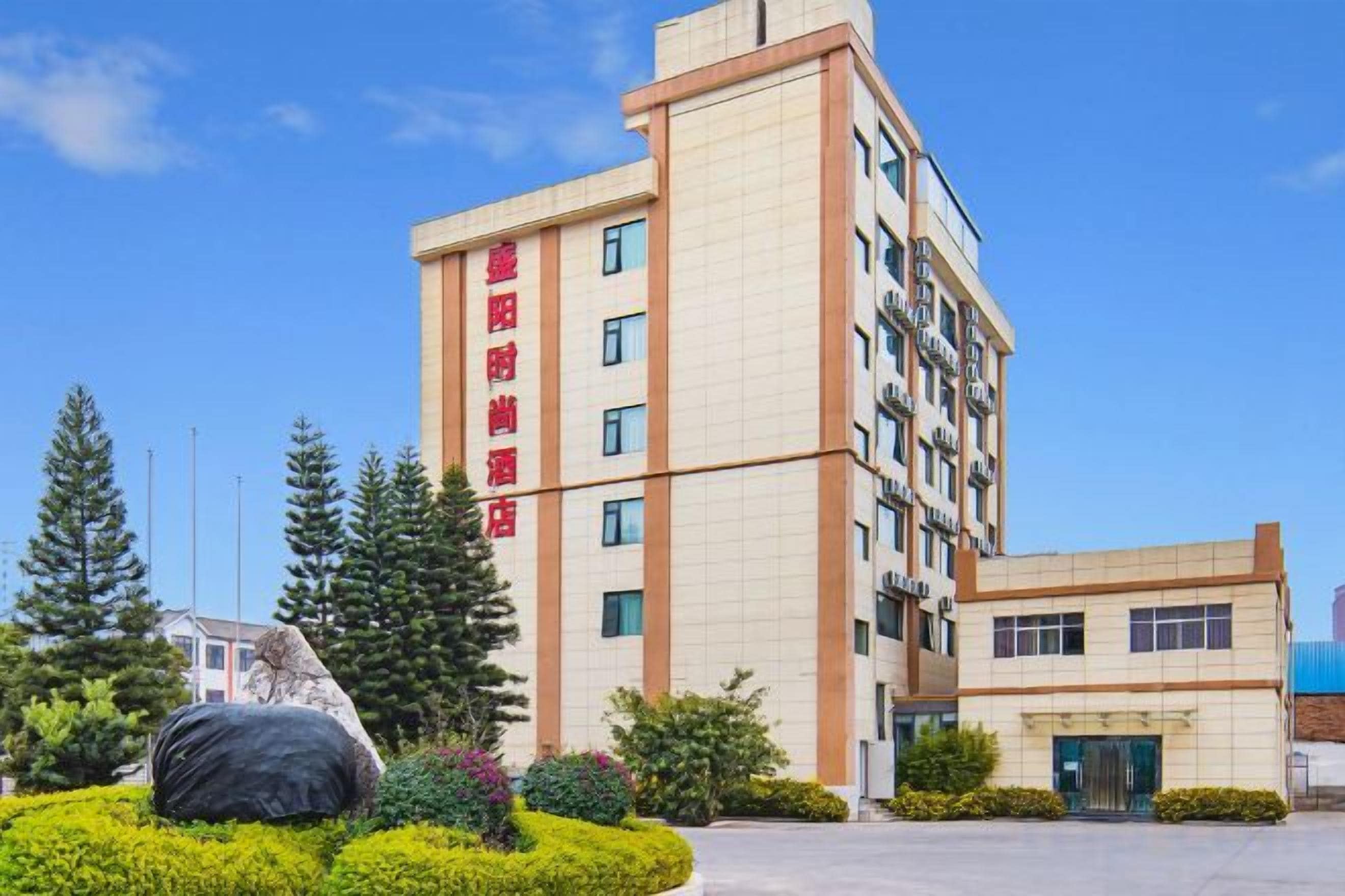 A multi-story hotel building with a prominent entrance and a landscaped area with a large rock feature.