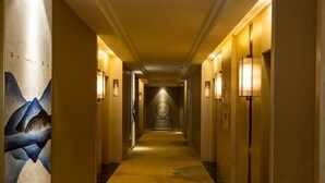 A hotel hallway with a carpeted floor, wall-mounted lamps, and a clock on the wall. - Shengyang Hotel (Yuxi)