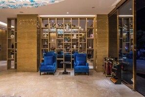 A lobby with a marble floor, two blue armchairs, a wooden bookshelf, and a glass storefront. - Shengyang Hotel (Yuxi)