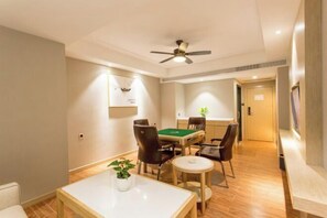 Habitación de hotel con comedor, ventilador de techo, mesa de billar verde y una pequeña mesa redonda con una planta.