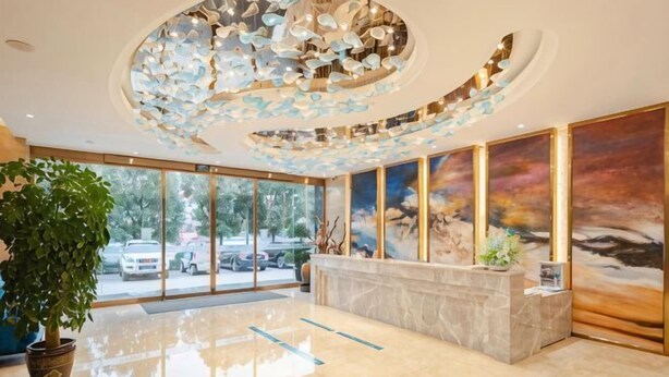 A hotel lobby with a reception desk, large windows, a decorative ceiling, and a large painting. - Shengyang Hotel (Yuxi)