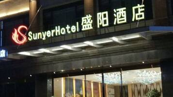 Entrada de hotel con señalización iluminada, amplias ventanas y diseño moderno.
