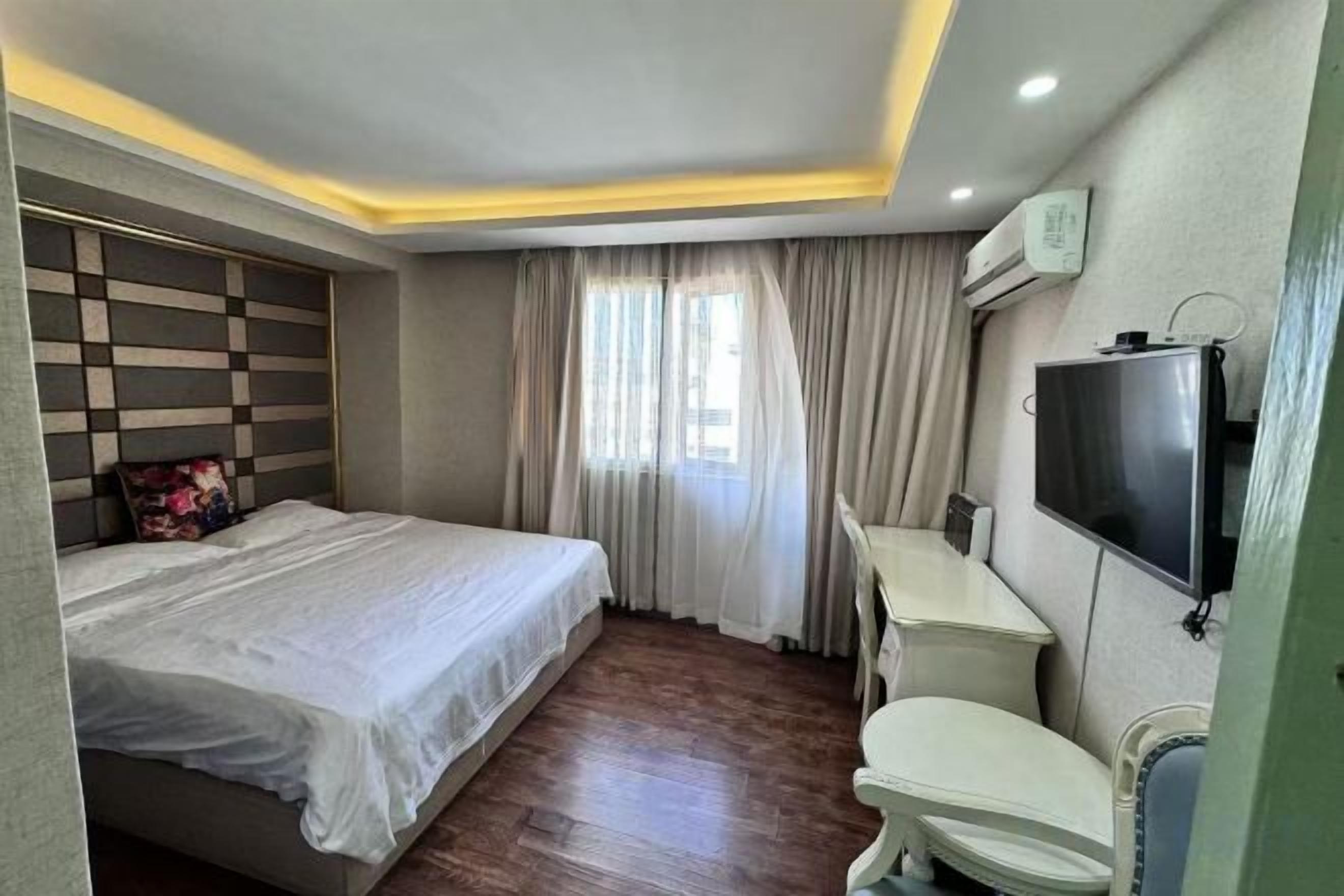 A hotel room with a bed, a desk, a chair, a television, and a window with curtains.