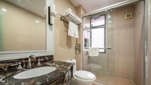 Un baño con lavamanos de mármol, inodoro y ducha con mampara de vidrio.