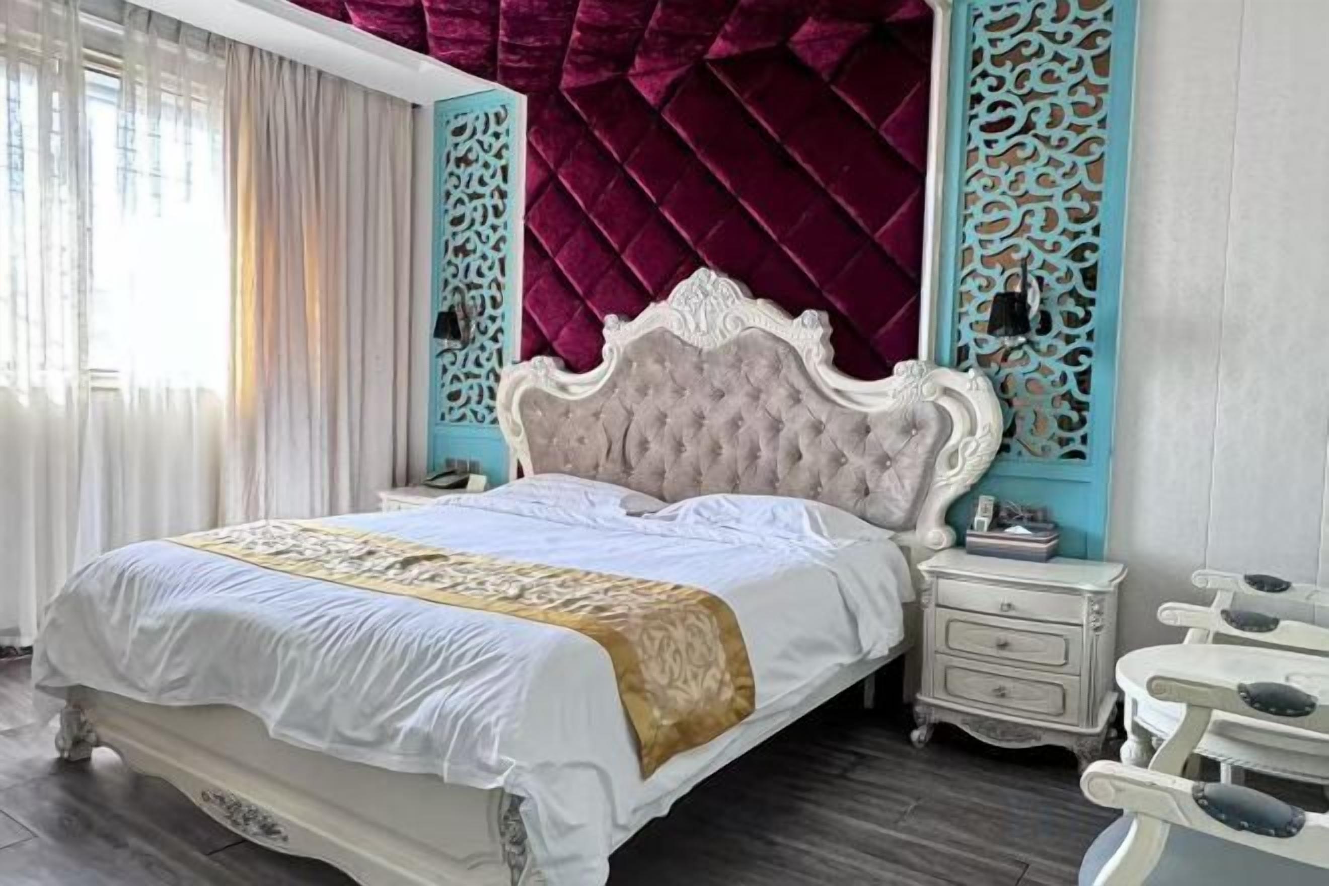 A bed with a white headboard and a gold accent, a nightstand with a lamp, and a blue decorative panel.