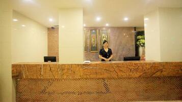 Un mostrador de recepción con encimera de mármol, una recepcionista y un papel tapiz decorativo al fondo.