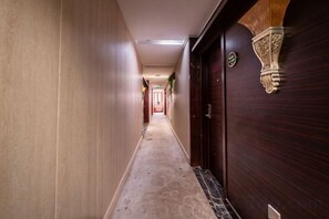 A hallway with a carpeted floor, a wooden door with a decorative handle, and a light fixture on the wall.
