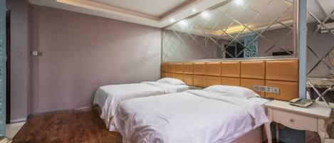 Habitación de hotel con dos camas, un espejo grande, piso de madera y una mesita de noche con lámpara.