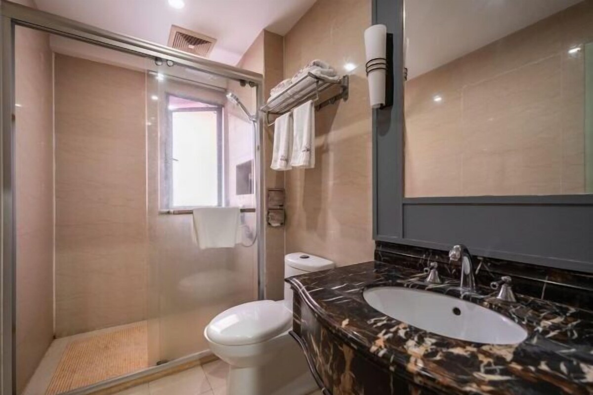 Une salle de bain avec une douche à parois de verre, des toilettes, un lavabo avec un plan de toilette en marbre et un porte-serviettes.