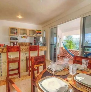 Un coin repas avec une table dressée pour quatre personnes, des chaises et une vue sur l’extérieur grâce à une porte vitrée.