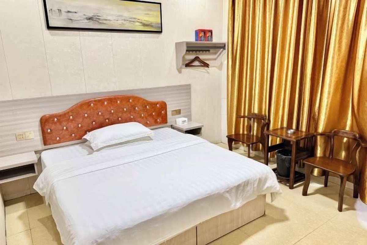A hotel room with a bed, bedside tables, a hanging light, a chair, and a curtain.