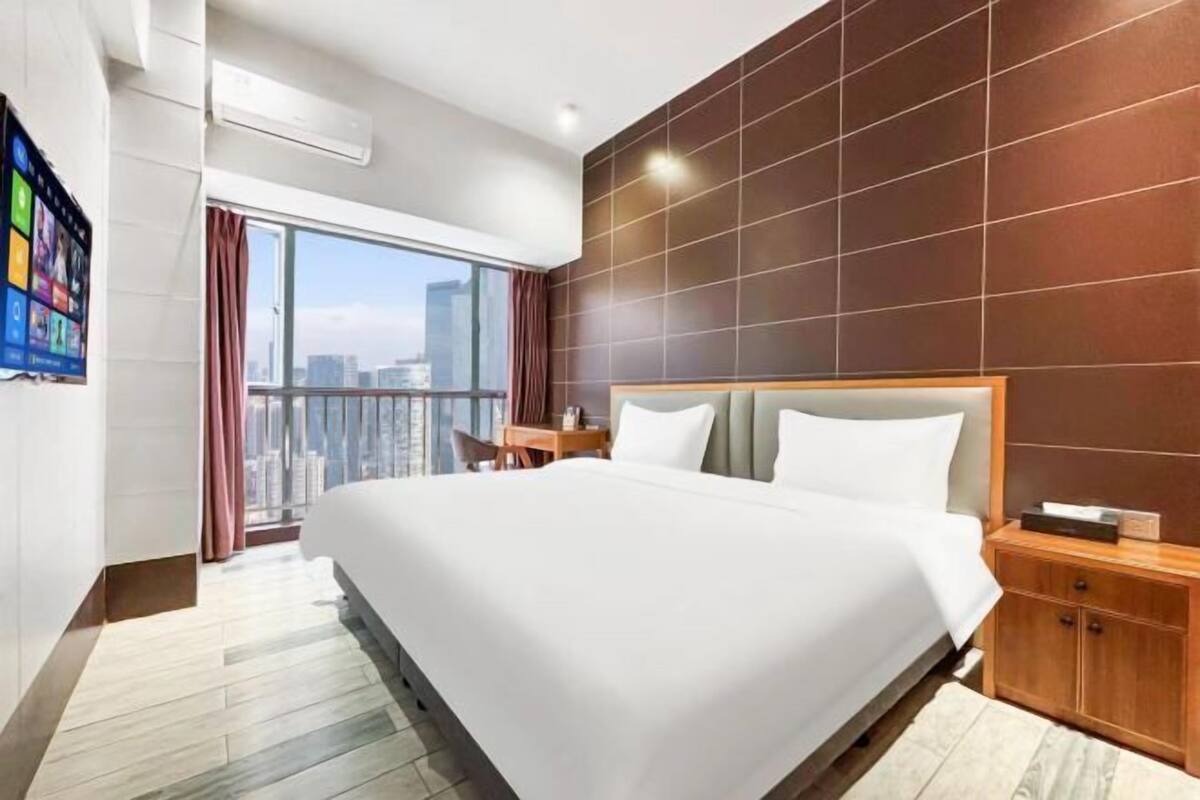 Una habitación de hotel moderna con una cama grande, cabecera de madera, mesita de noche y vistas a la ciudad.