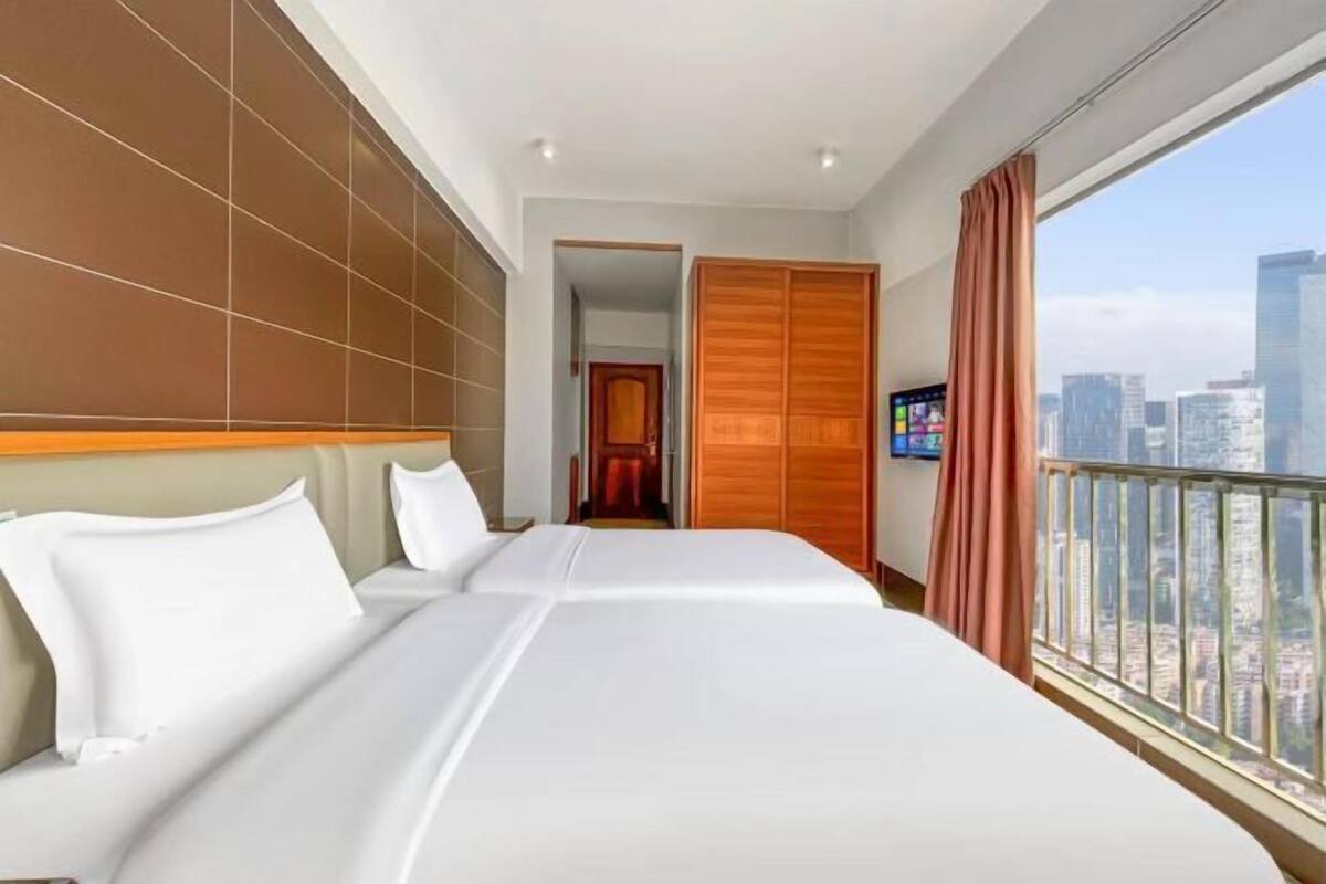 Habitación de hotel con una cama grande, televisión y vista a la ciudad.
