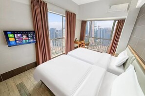 Habitación de hotel con dos camas, un televisor montado en la pared, un balcón con vistas a la ciudad y un escritorio con una silla.
