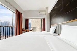 A hotel room with a large bed, a view of the city, and a balcony with curtains.