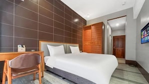 A modern hotel room with a large bed, a wooden desk, a chair, and a TV mounted on the wall. - Green Leaf Inn (Dongguan)
