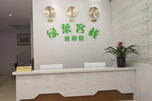 A reception desk with a clock, a potted plant, and a sign. - Green Leaf Inn (Dongguan)