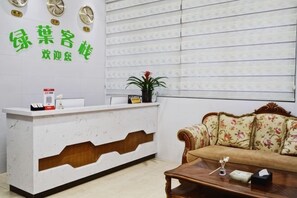 A reception desk with a floral couch and a wooden coffee table in the foreground. - Green Leaf Inn (Dongguan)