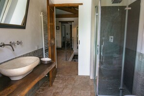Une salle de bain avec un lavabo en pierre, une douche et un banc en bois.