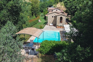 Un bâtiment en pierre doté d’une piscine, entouré d’une végétation luxuriante.