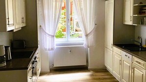 A kitchen with white cabinets, a window with sheer curtains, a radiator, and a wooden floor. - Large stylishly furnished holiday flat in a quiet and central location (Weimar)