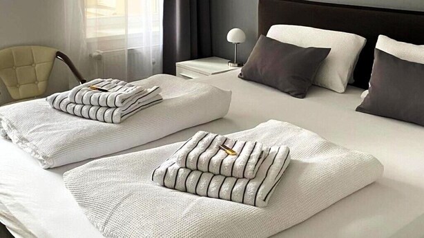 A neatly made bed with folded towels and pillows, a bedside table with a lamp, and a chair in a hotel room. - Large stylishly furnished holiday flat in a quiet and central location (Weimar)