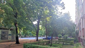 Un parc avec des arbres, un terrain de sport bleu et un bâtiment couvert de graffitis.