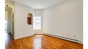 Una habitación con piso de madera, paredes blancas y un ventanal pequeño.